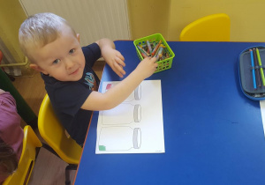 Chłopiec wykonuje ćwiczenie związane z owocami i warzywami.